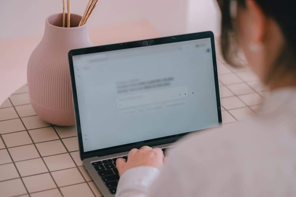Pessoa digita no laptop numa tela de assistente de IA com caixa de pergunta, ao lado de um vaso rosa