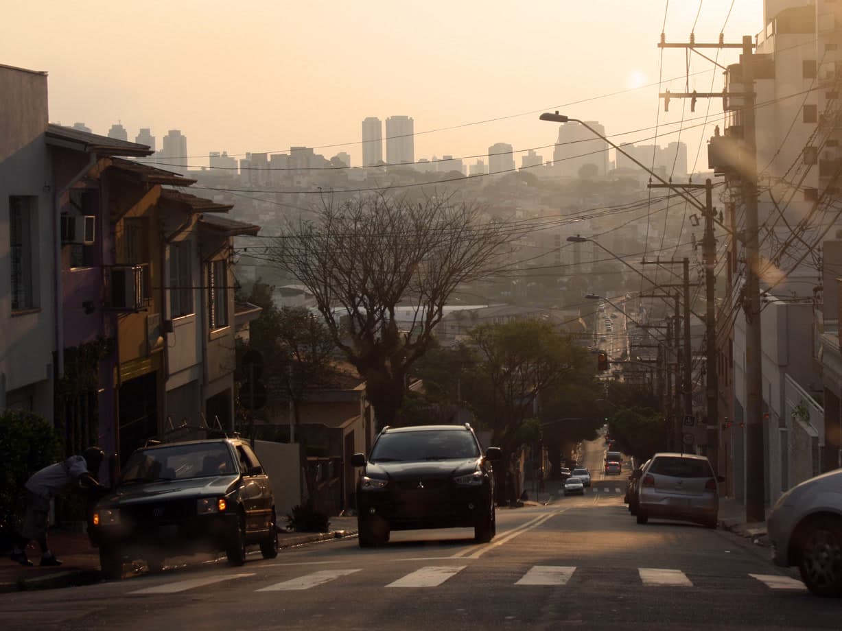 Rua de São Caetano do Sul no fim da tarde, com os prédios de São Paulo na neblina ao fundo